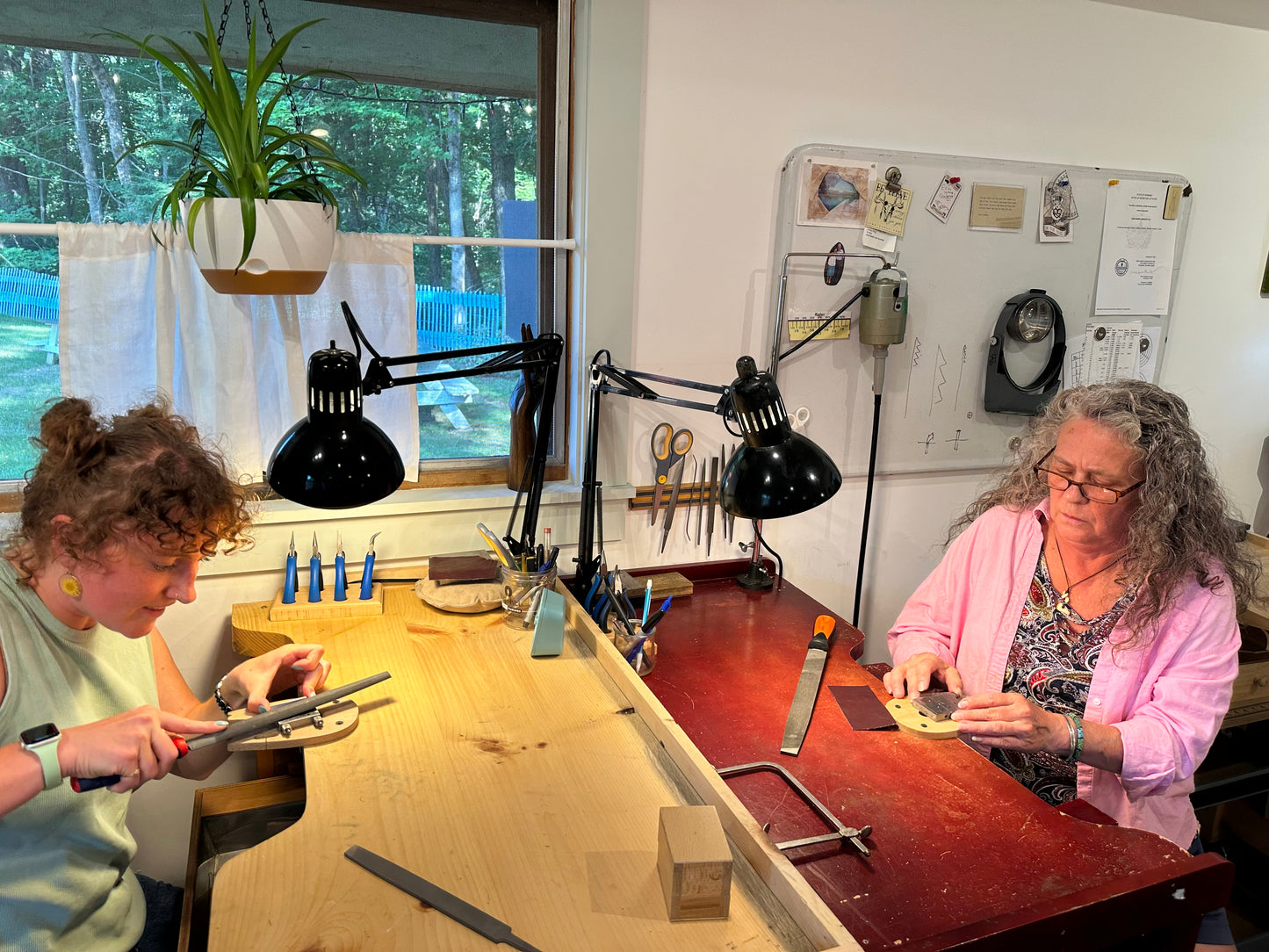 Two women working at a table with tools and materials in a workshop setting.