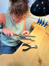 Load image into Gallery viewer, Person using a tool on a wooden surface with tools hanging on the wall.